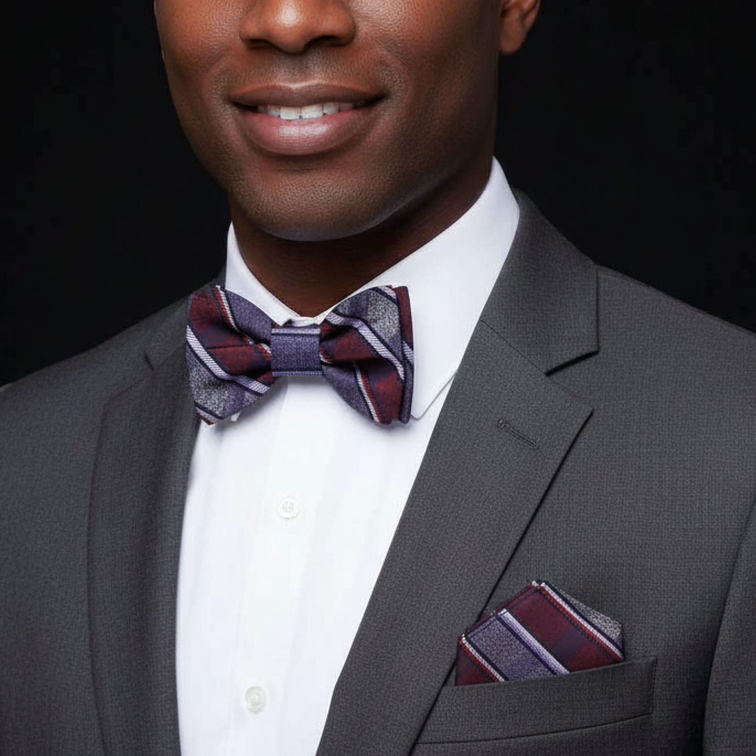 Man wearing a gray suit with a red bow tie and pocket square on a black background
