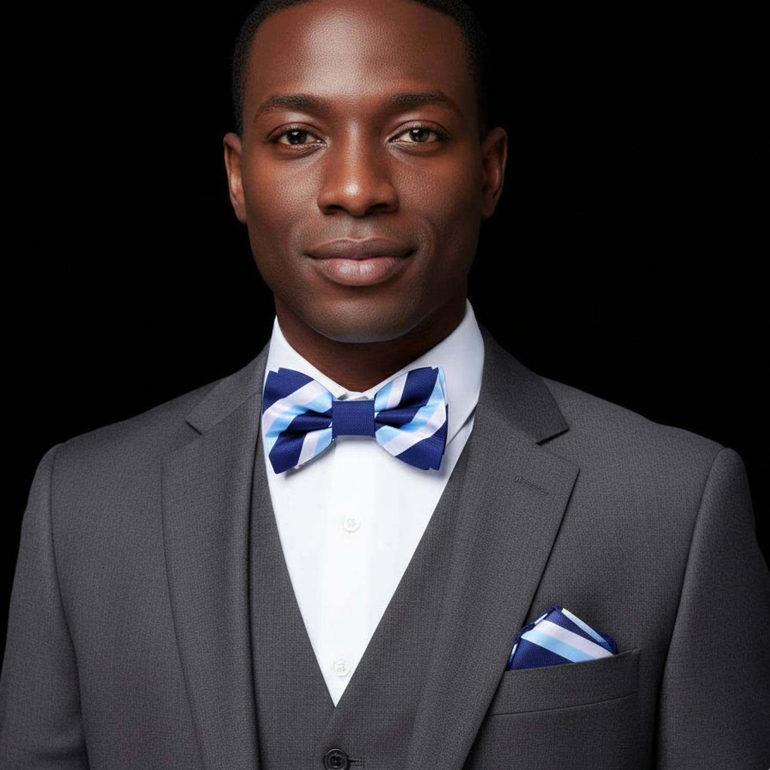 Man wearing a gray suit with a blue and white striped bow tie and pocket square on a black background
