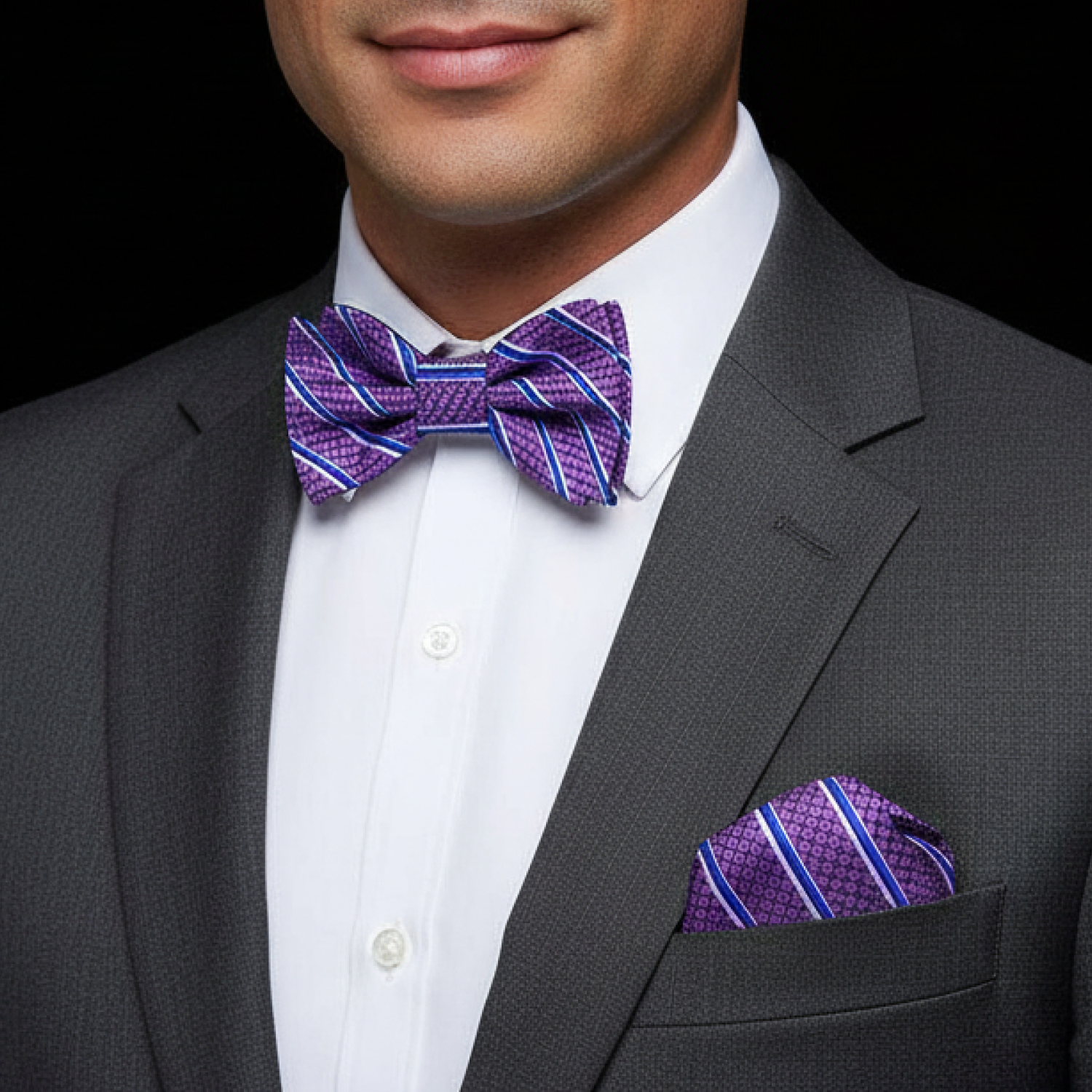 Man wearing a gray suit with a purple striped bow tie and pocket square on a black background