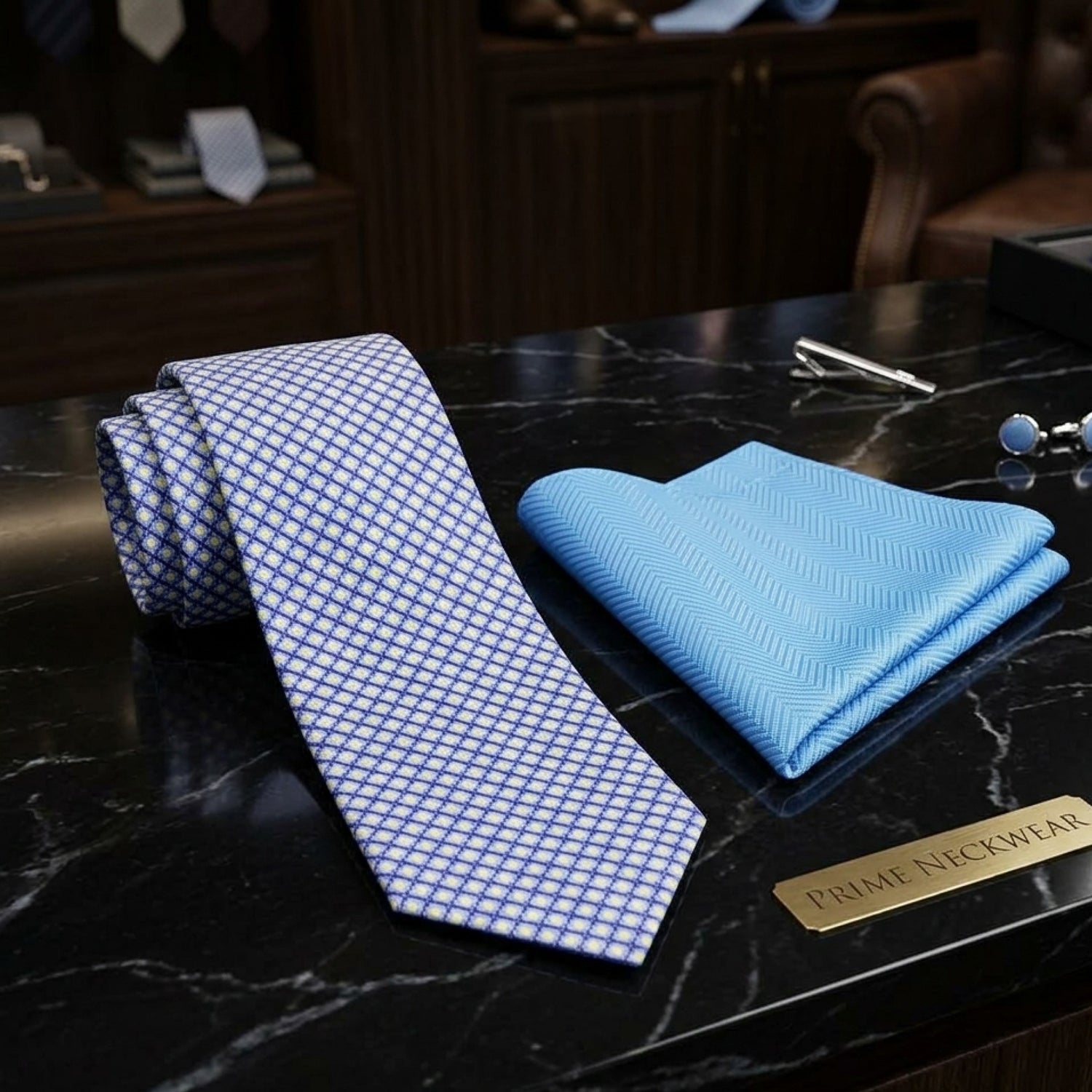 A men's necktie and pocket square set displayed on a black marble surface. The necktie is light blue with a small white geometric grid pattern, and the matching pocket square is a solid light blue.