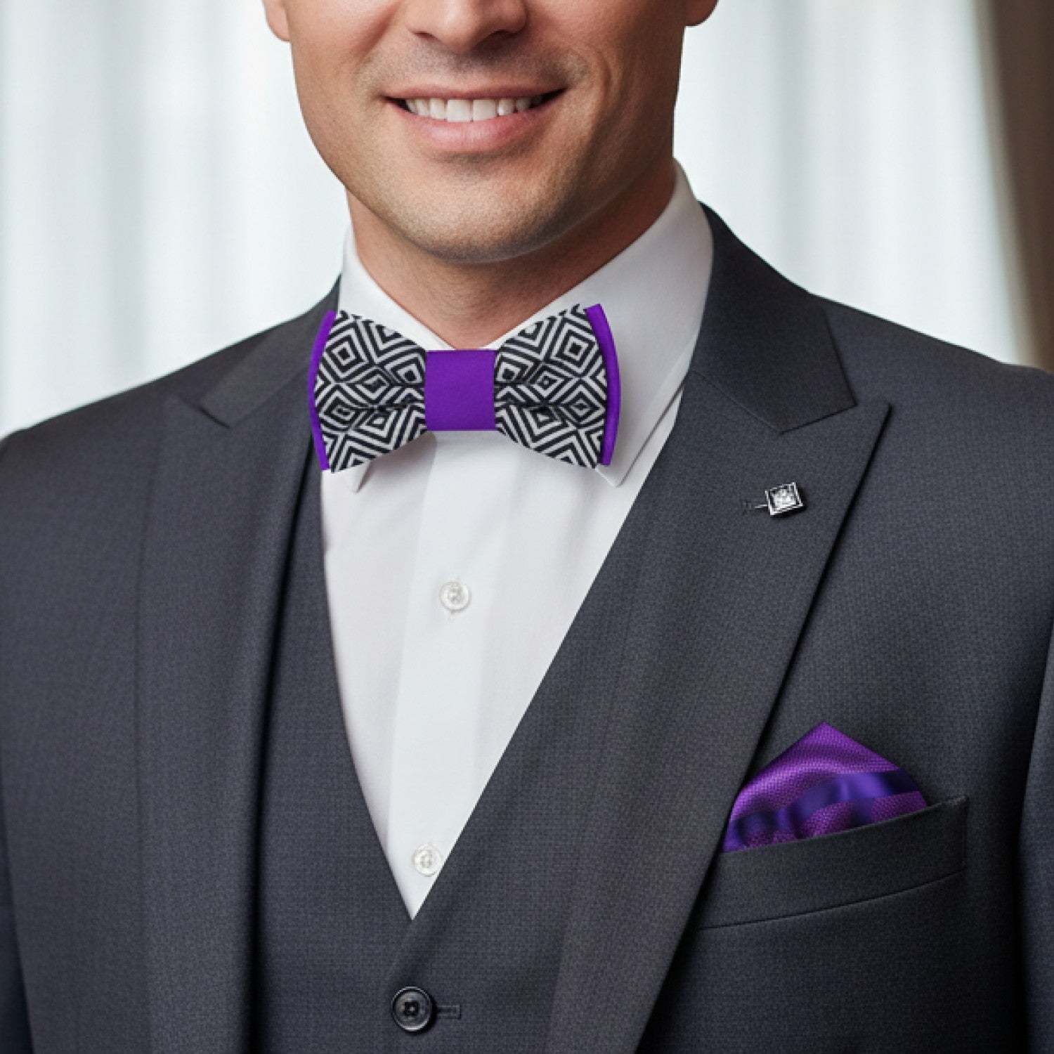 Man wearing a gray suit with a purple bow tie and pocket square against a white curtain background