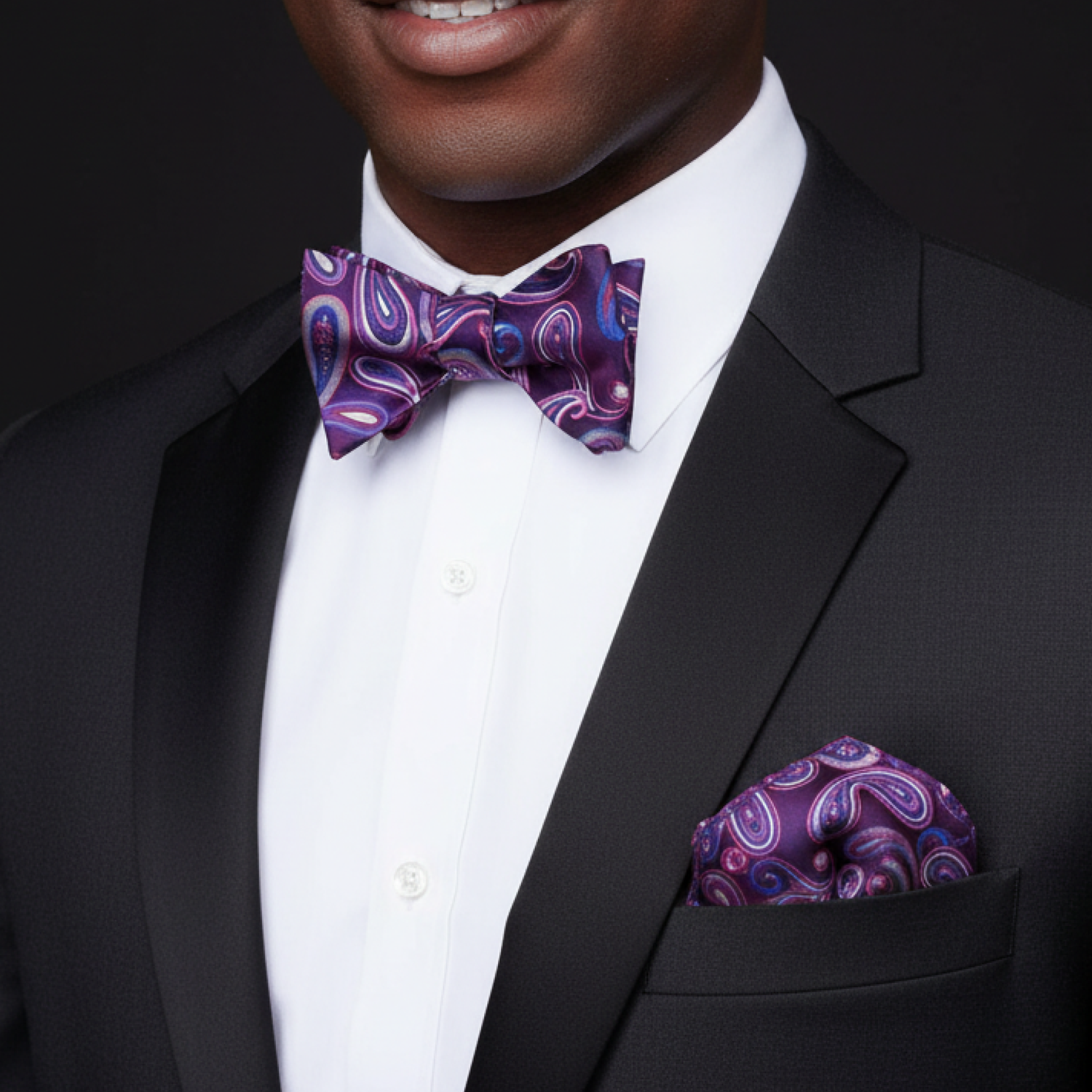 Man wearing a black suit with a purple paisley bow tie and pocket square.