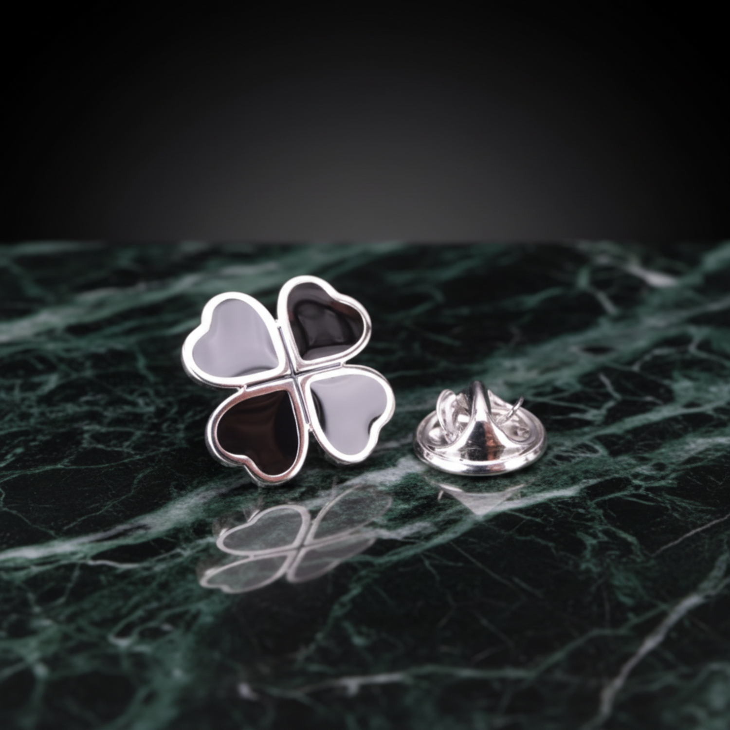 A silver four-leaf clover lapel pin with heart-shaped sections, shown open with a separate metal clutch backing on a black reflective background.