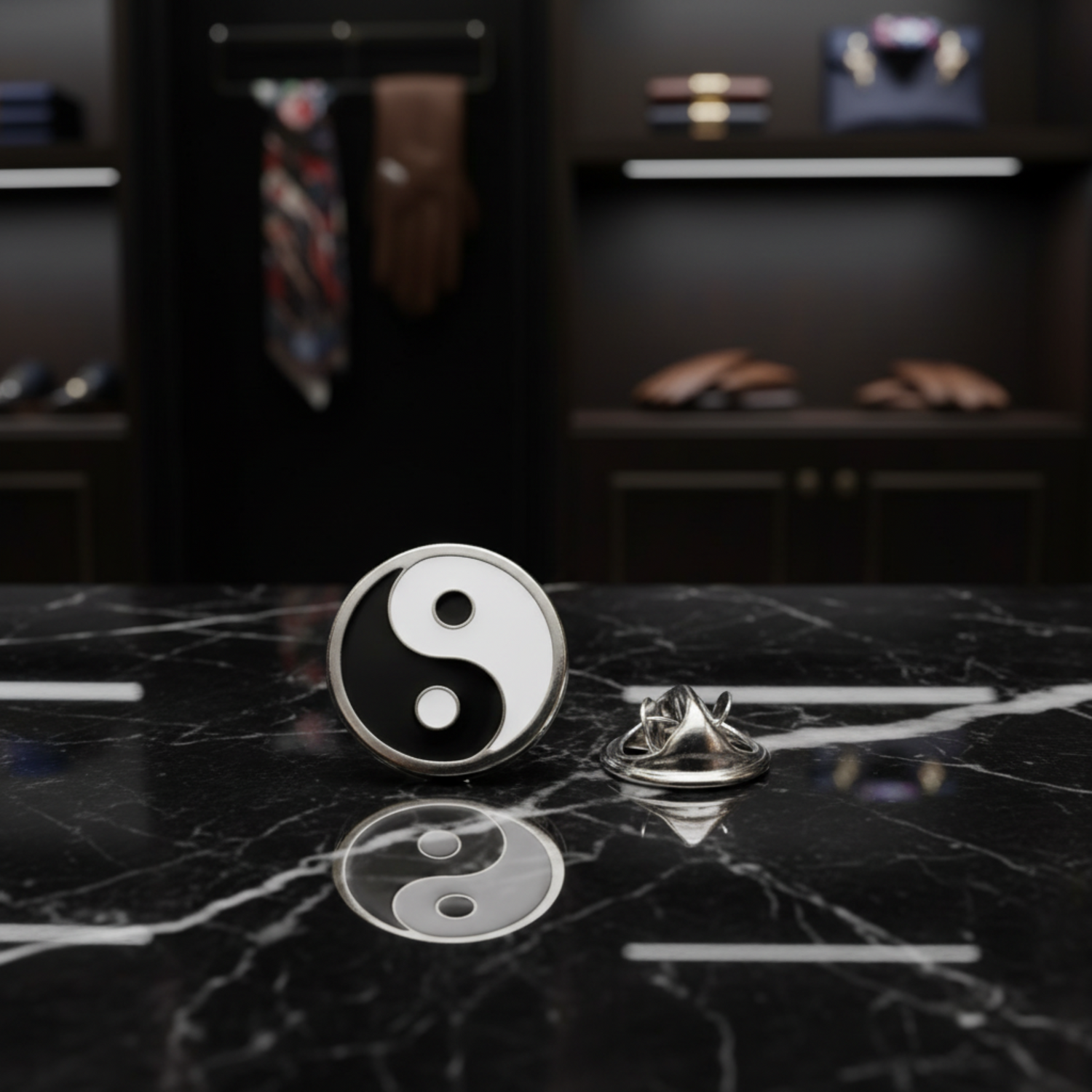 A pair of round silver lapel pins featuring a black and white yin-yang symbol, with one pin showing the front design and the other showing the metal backing, set against a reflective black background. 
