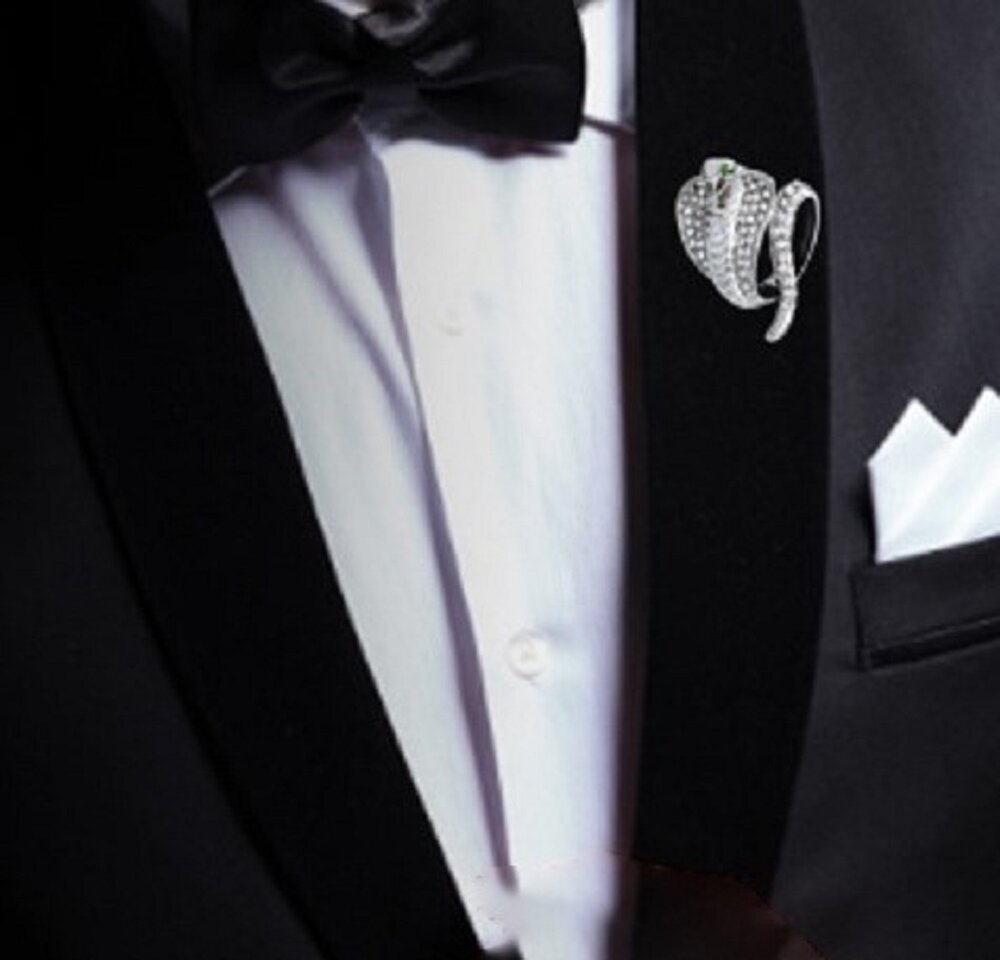 A gold colored with clear stones cobra shaped lapel pin on a suit with bow tie, white lapel pin and white shirt combo